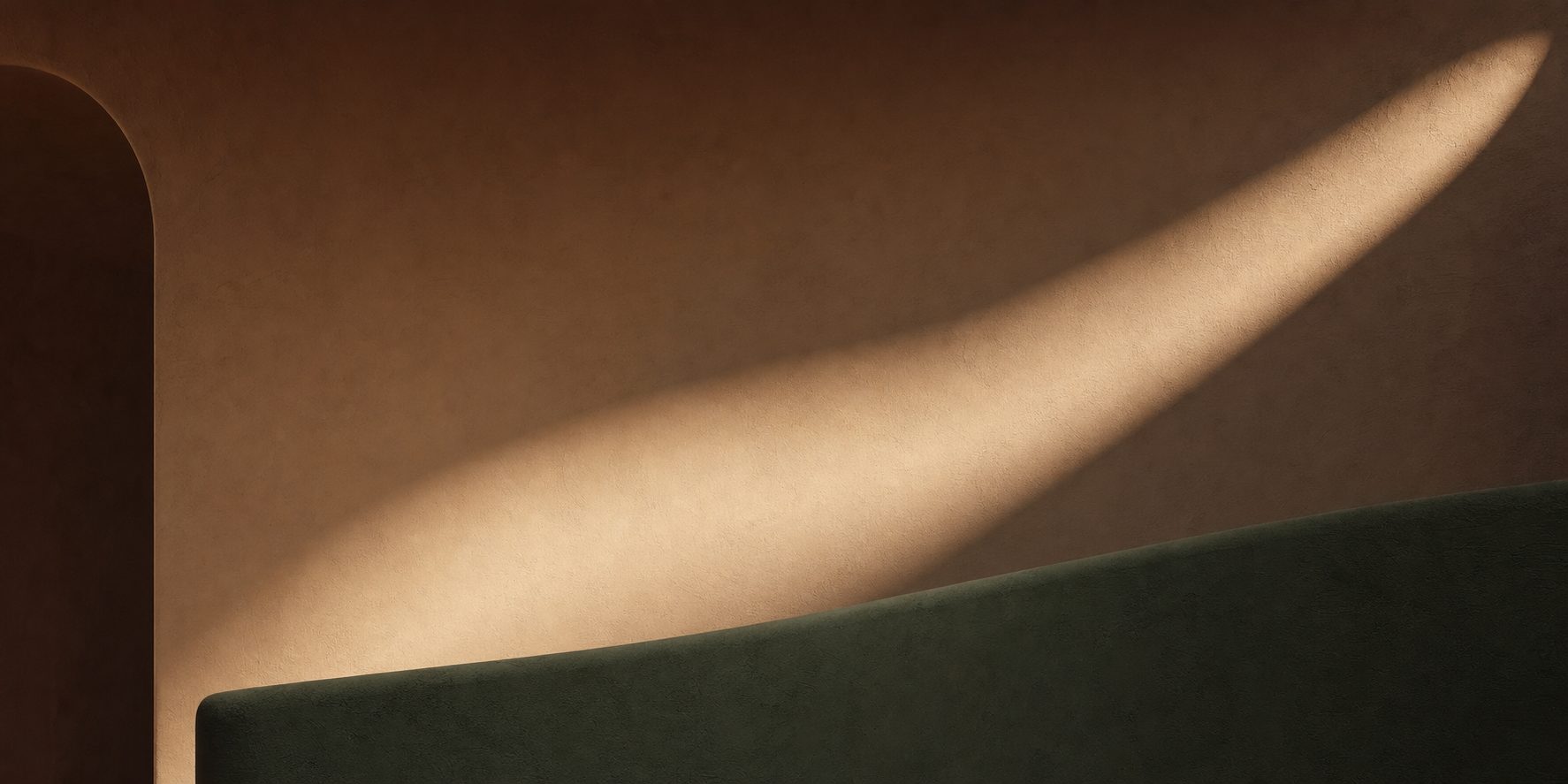 A soft curve of warm light crossing a plaster wall above a deep green form.
